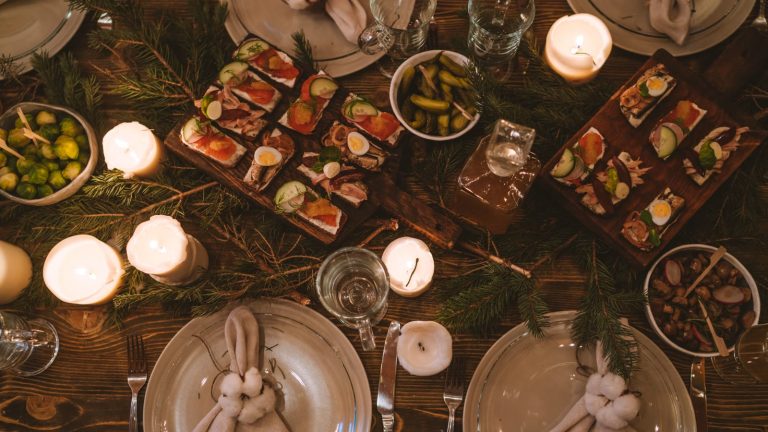 Julefrokostbord dækket med smørrebrød, levende lys og grangrene set ovenfra